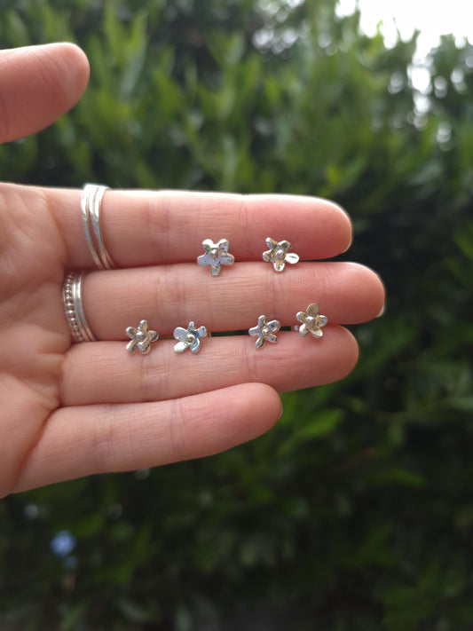 Silver flower-shaped earrings held in a hand with a blurred green background