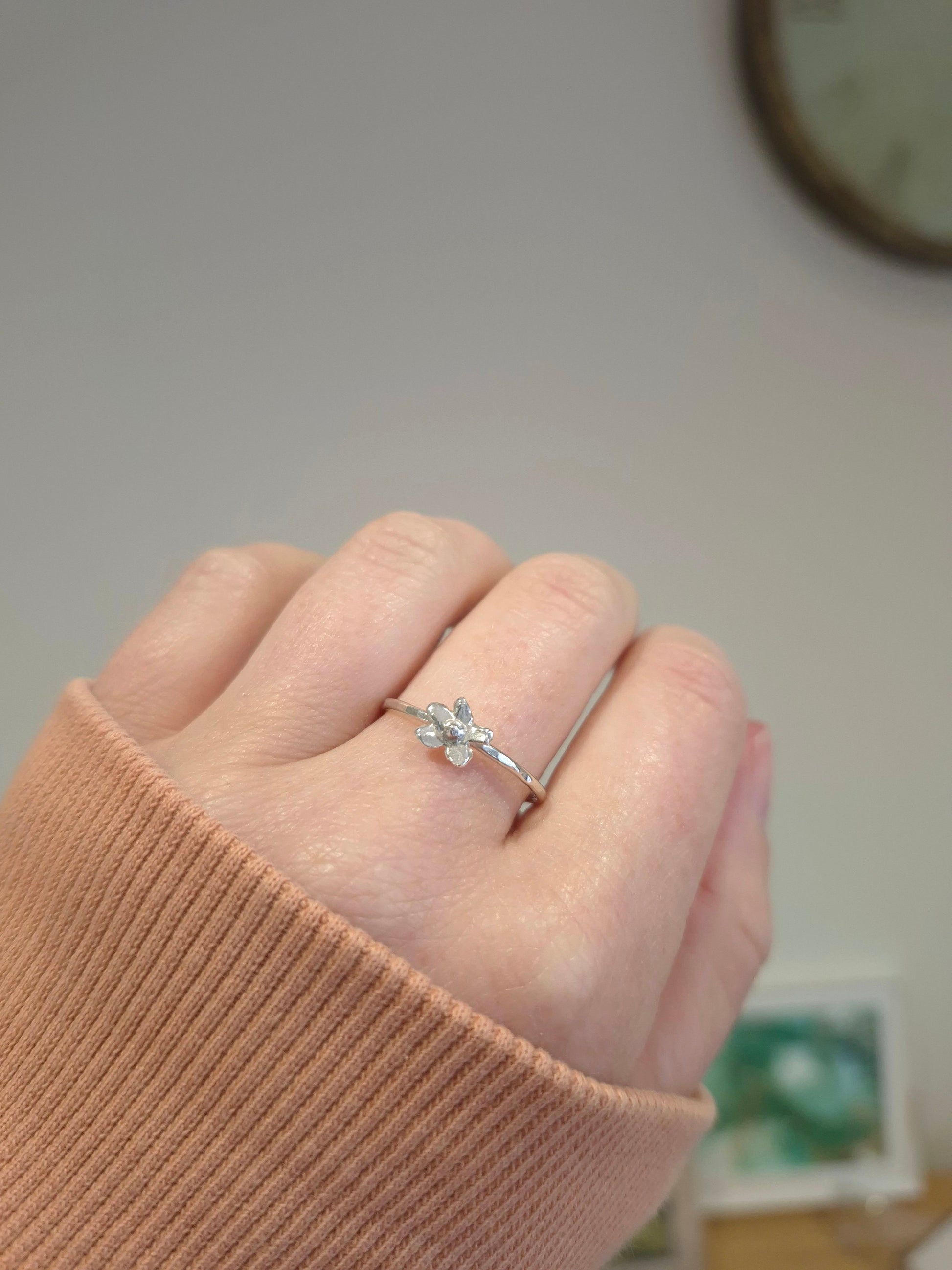 Hand wearing a silver ring with a floral design on a neutral background