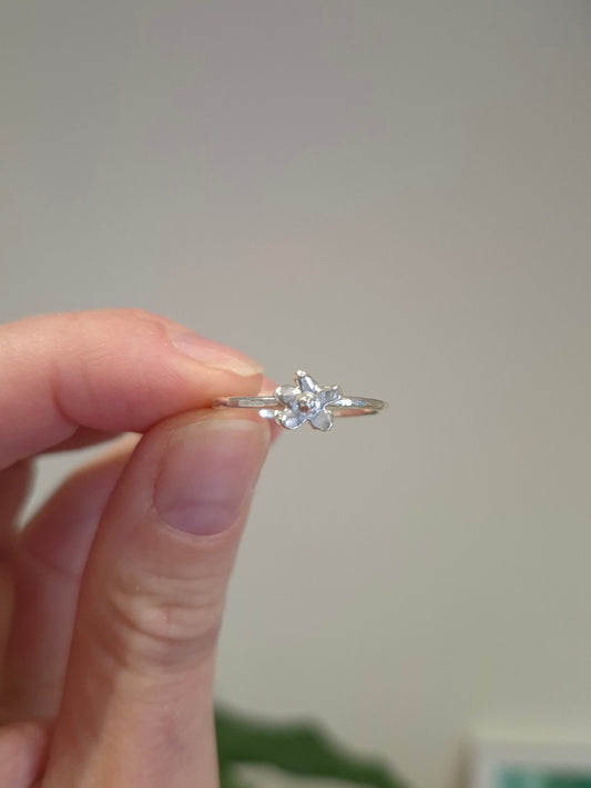 Silver ring with a diamond held between fingers against a neutral background