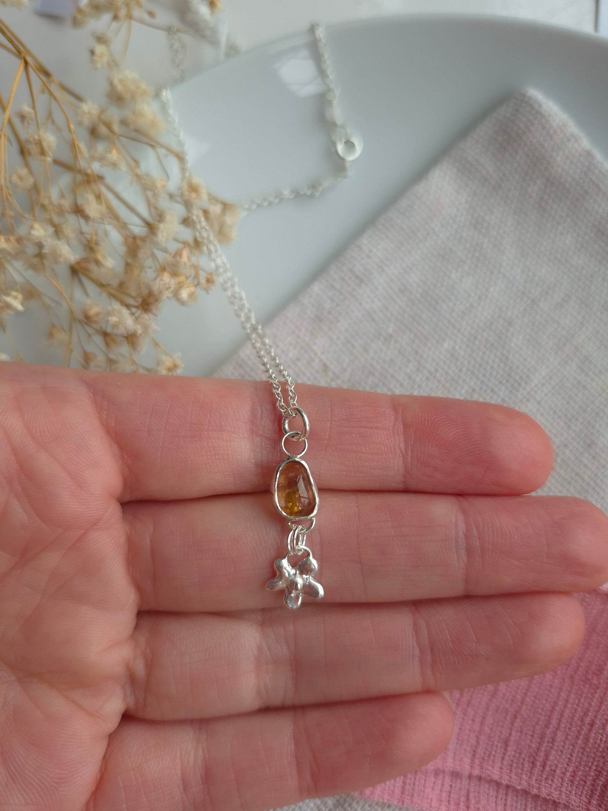 Silver necklace with a pendant held in a hand, with a blurred background