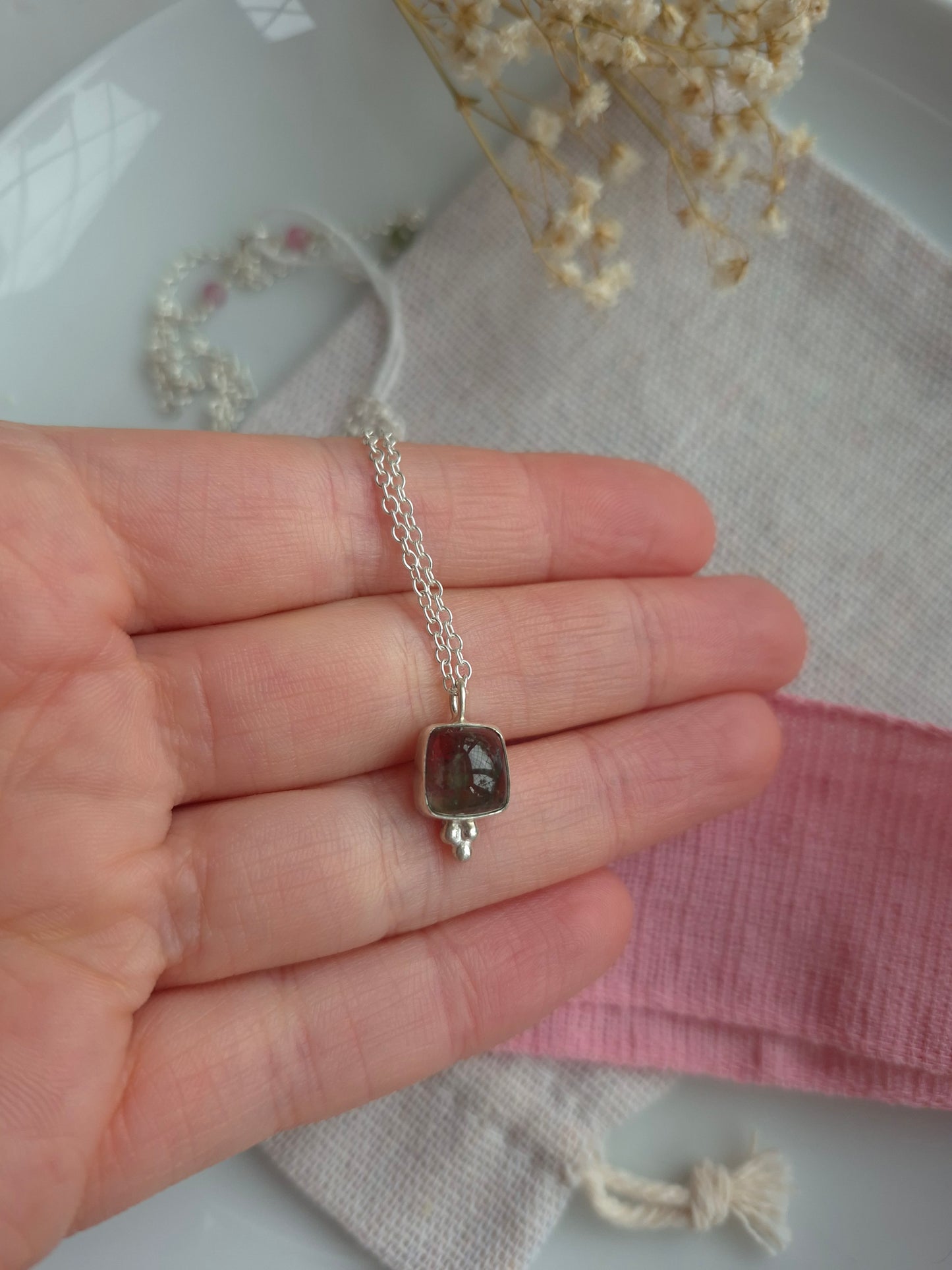 Silver necklace with a pendant held in a hand against a soft background