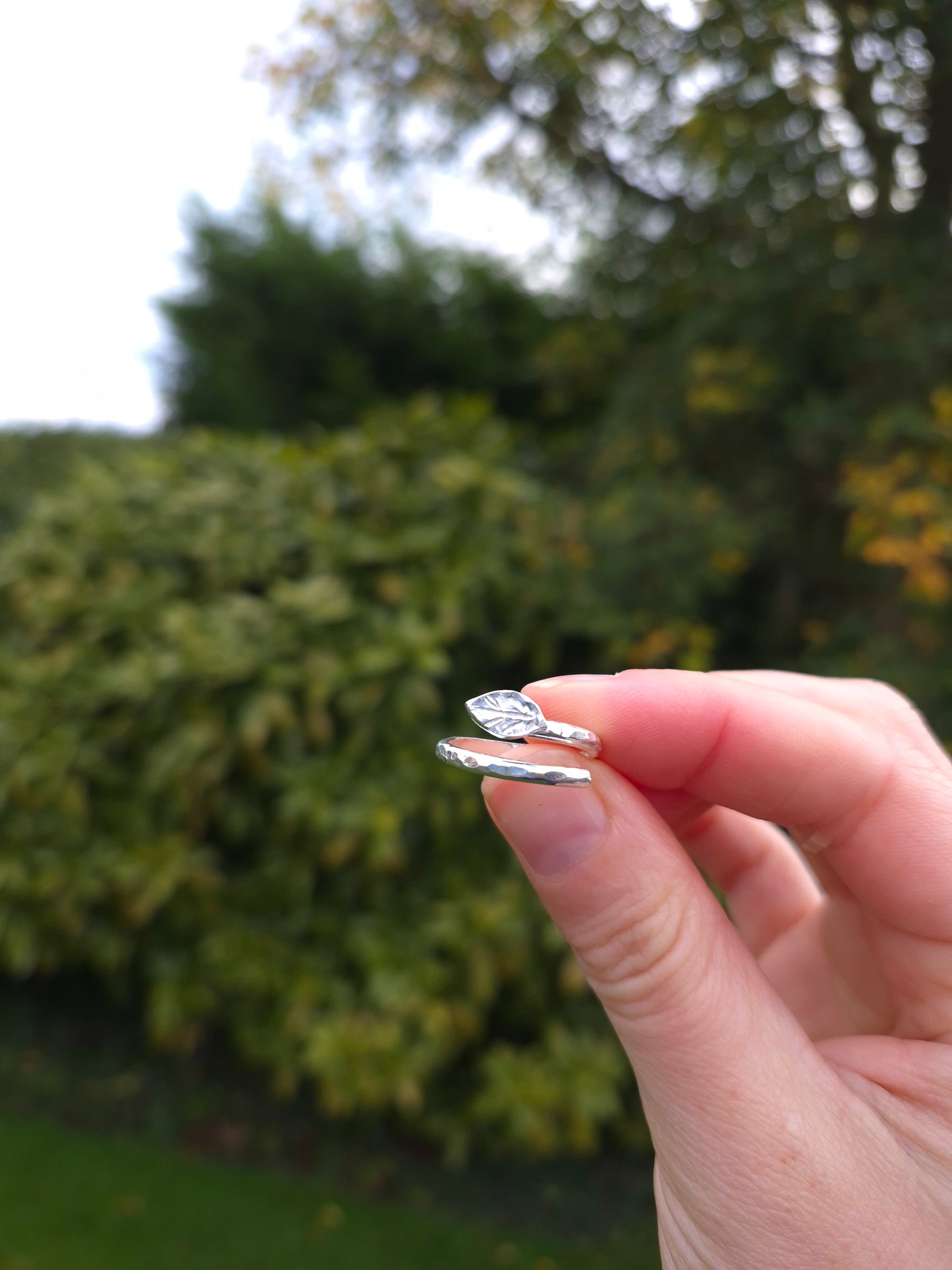 Hand holding a silver ring with a blurred green outdoor background