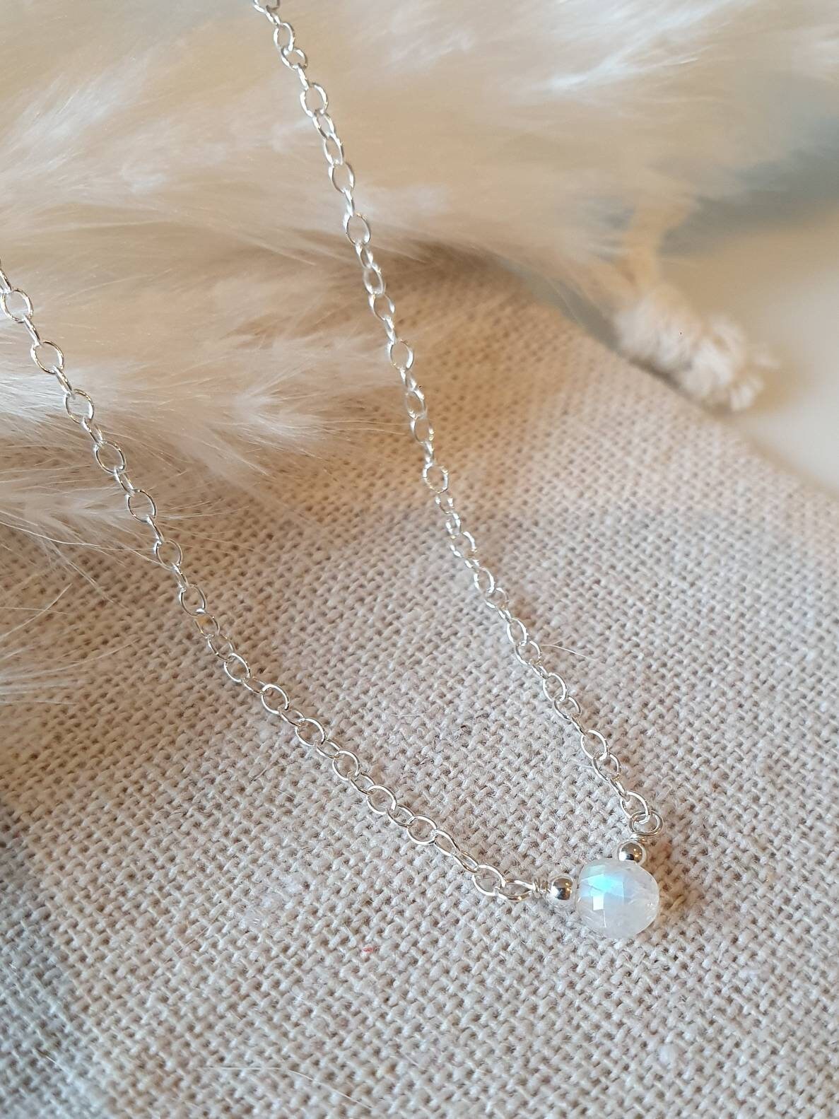 Delicate silver chain necklace with a small pendant on a textured beige surface