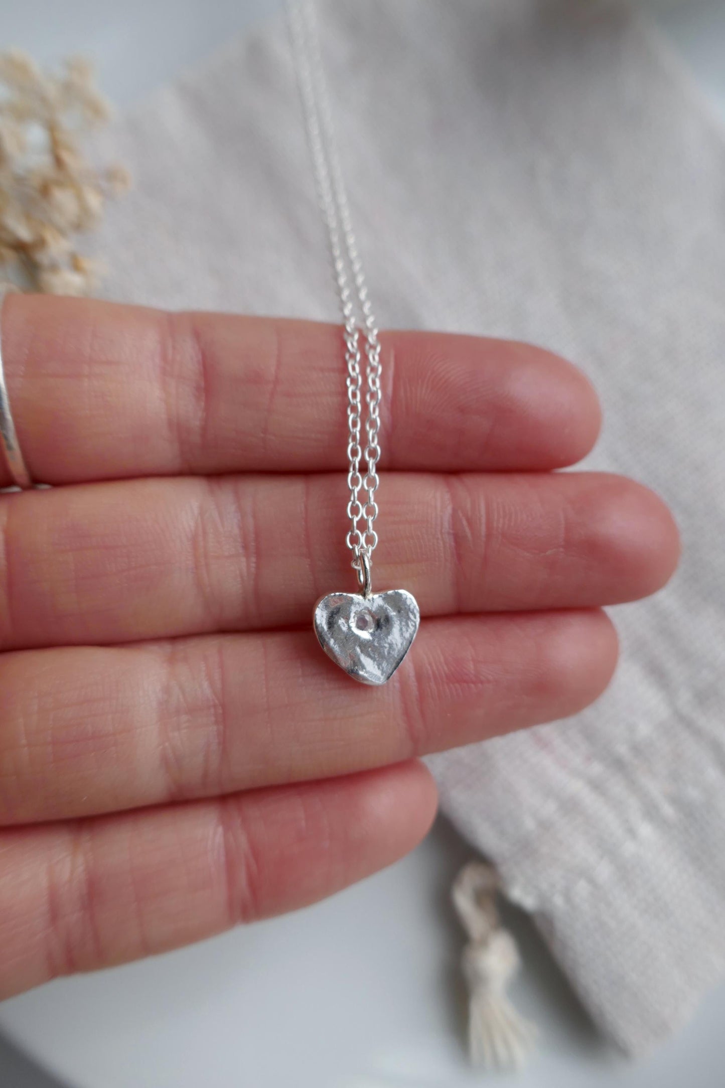 Silver heart-shaped pendant necklace held between fingers on a light background