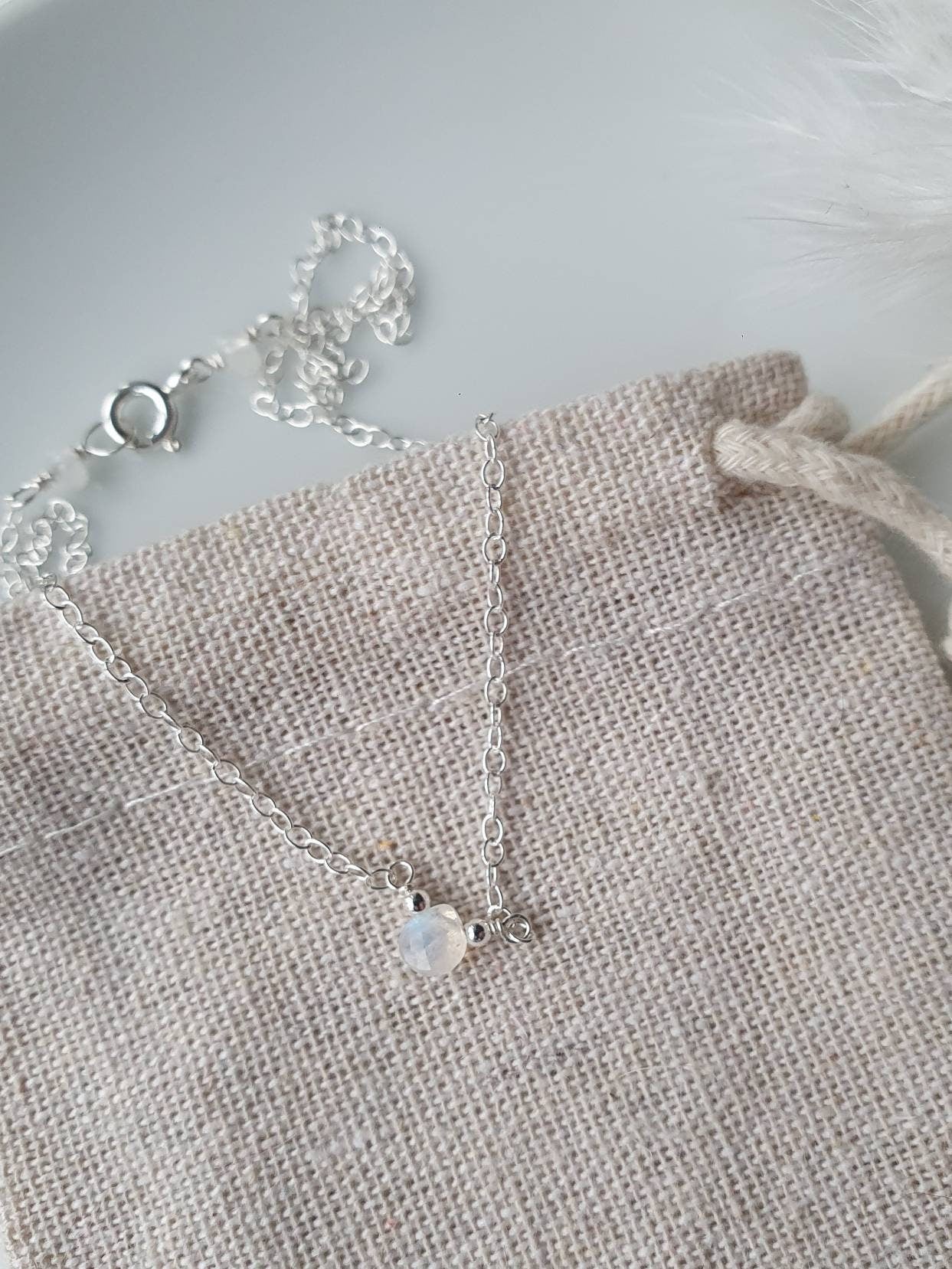 Silver necklace with a small pendant on a textured beige surface