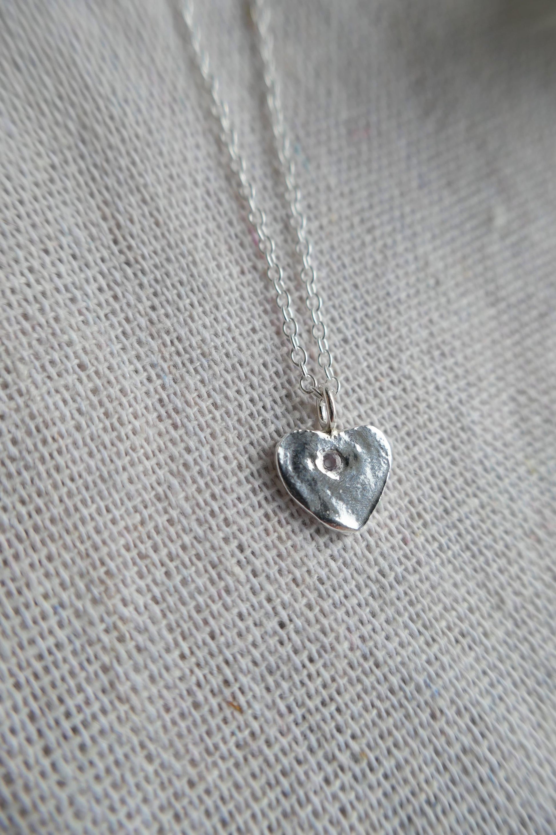 Silver heart-shaped pendant on a chain against a textured gray background
