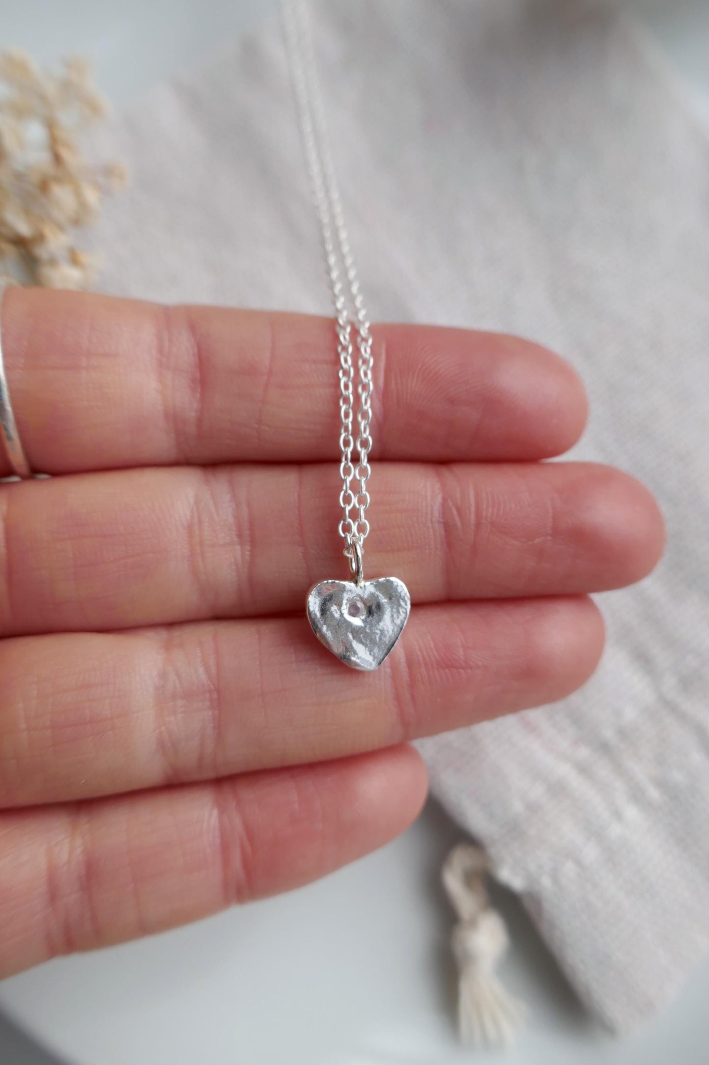 Silver heart-shaped pendant necklace held between fingers on a light background