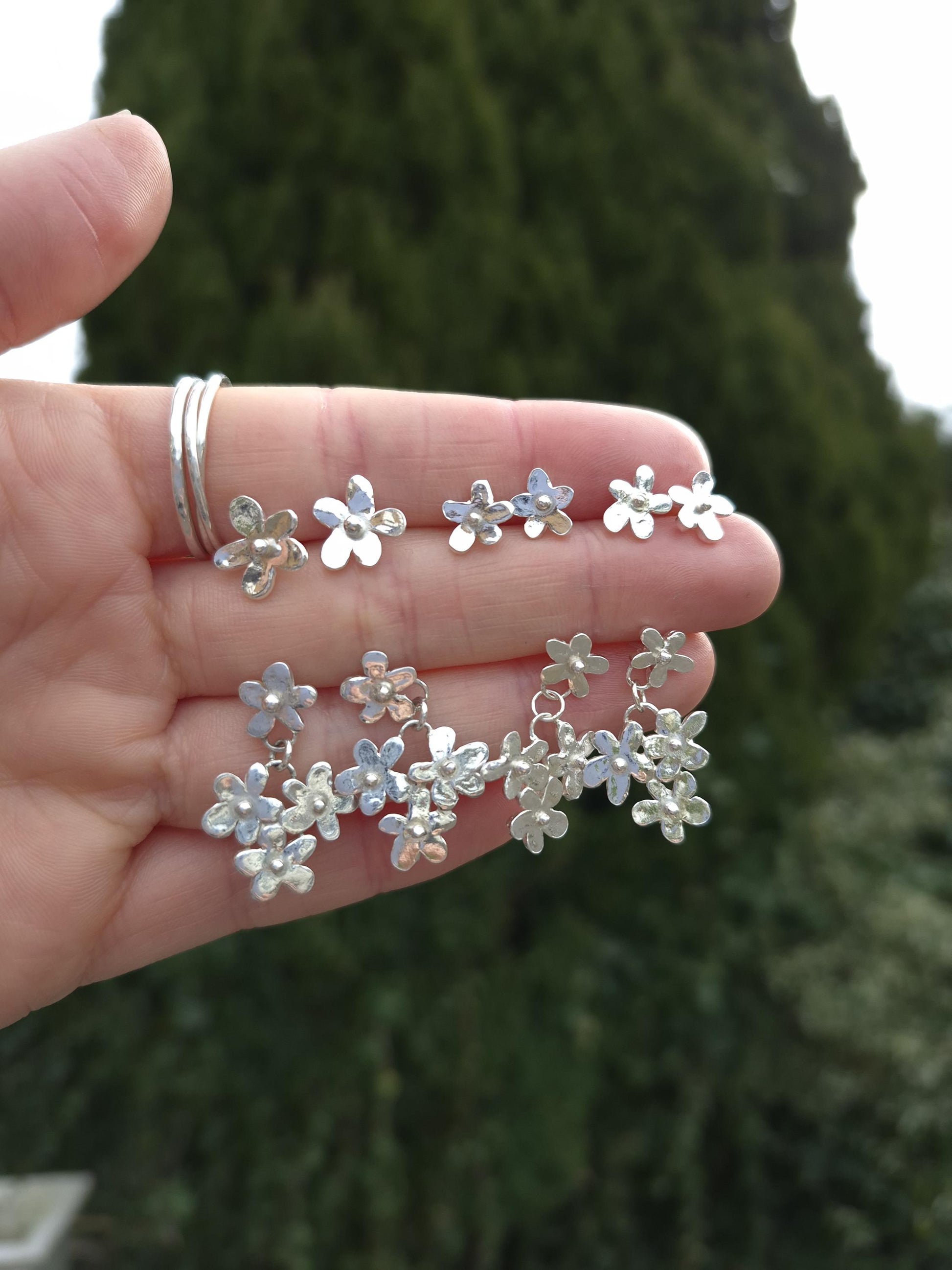 Silver floral earrings held in a hand with a blurred green background