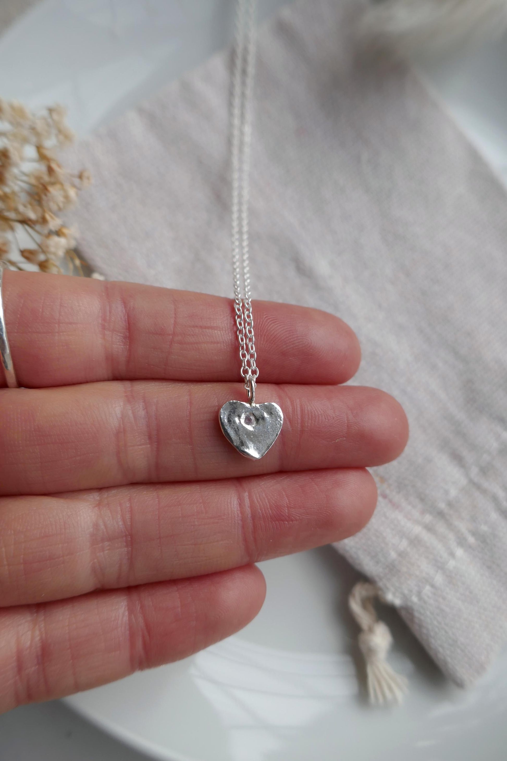 Silver heart-shaped pendant necklace held between fingers on a light background