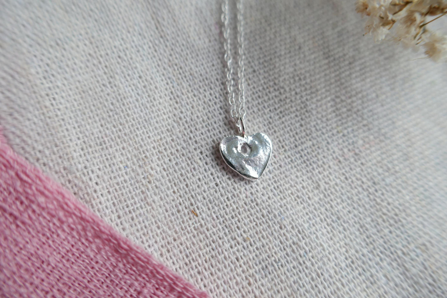 Silver heart-shaped pendant necklace on a textured fabric background