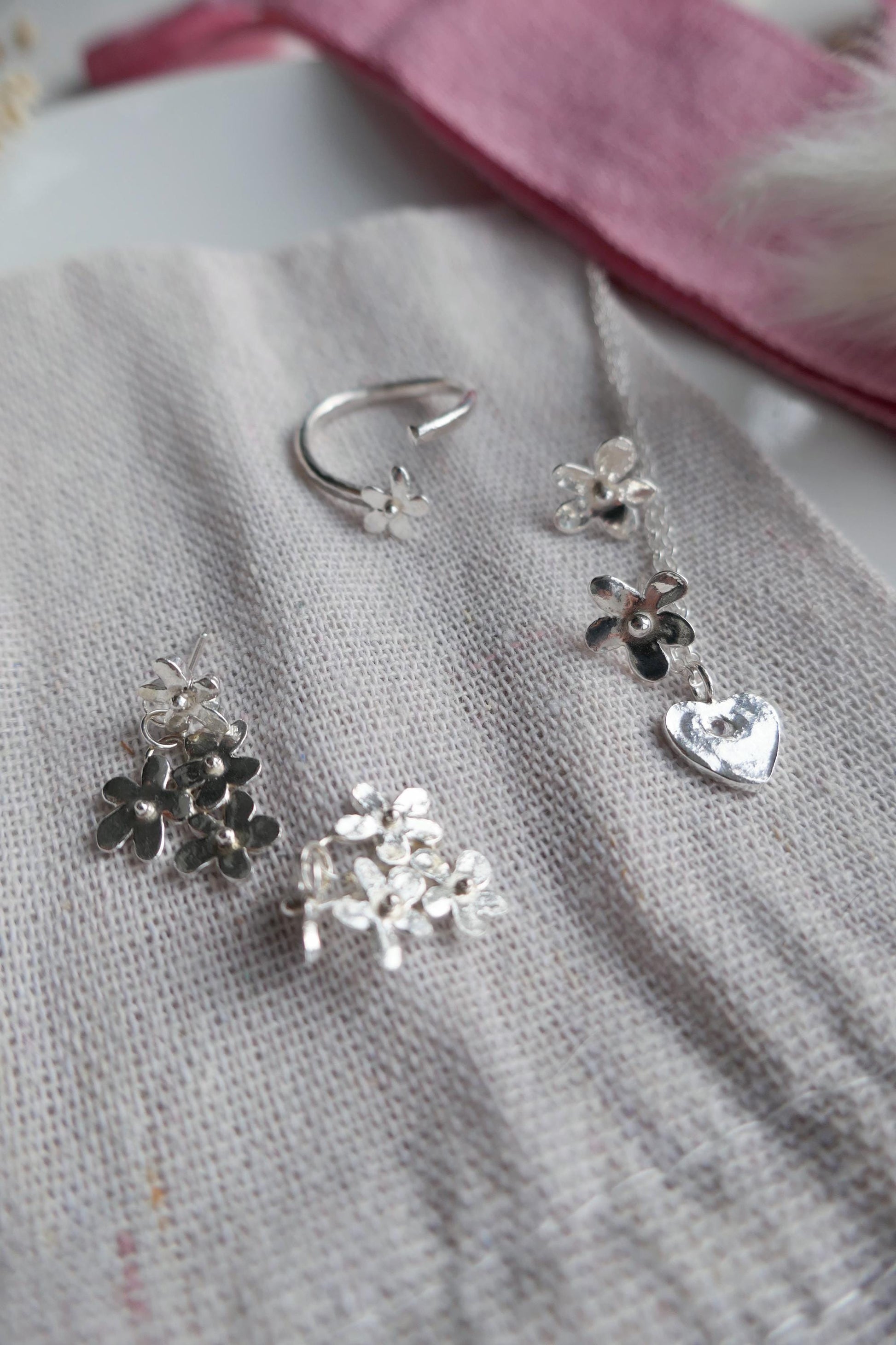 Silver earrings with floral and heart designs on a textured fabric background