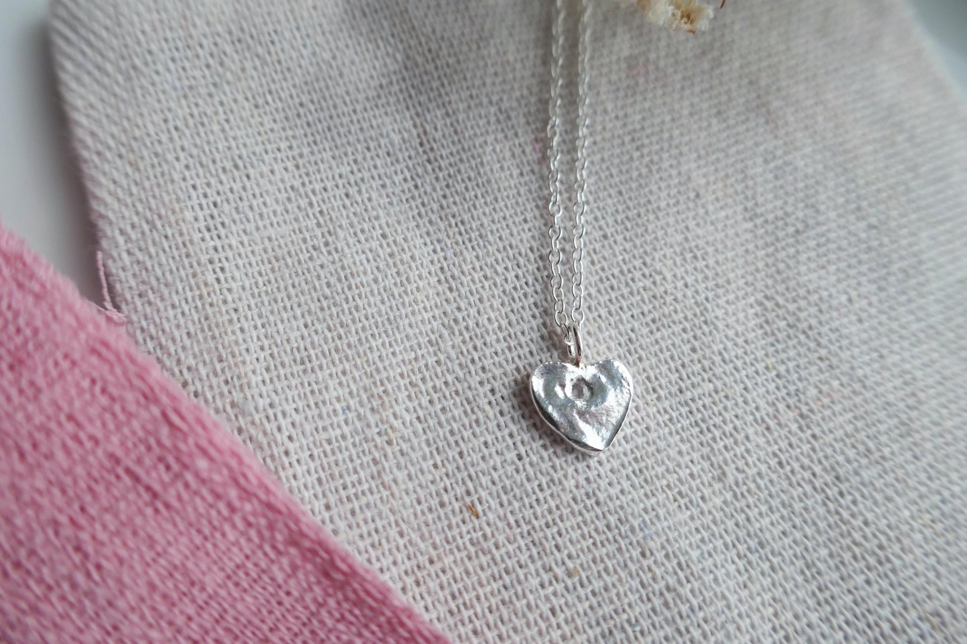 Silver heart-shaped pendant on a chain against a textured fabric background