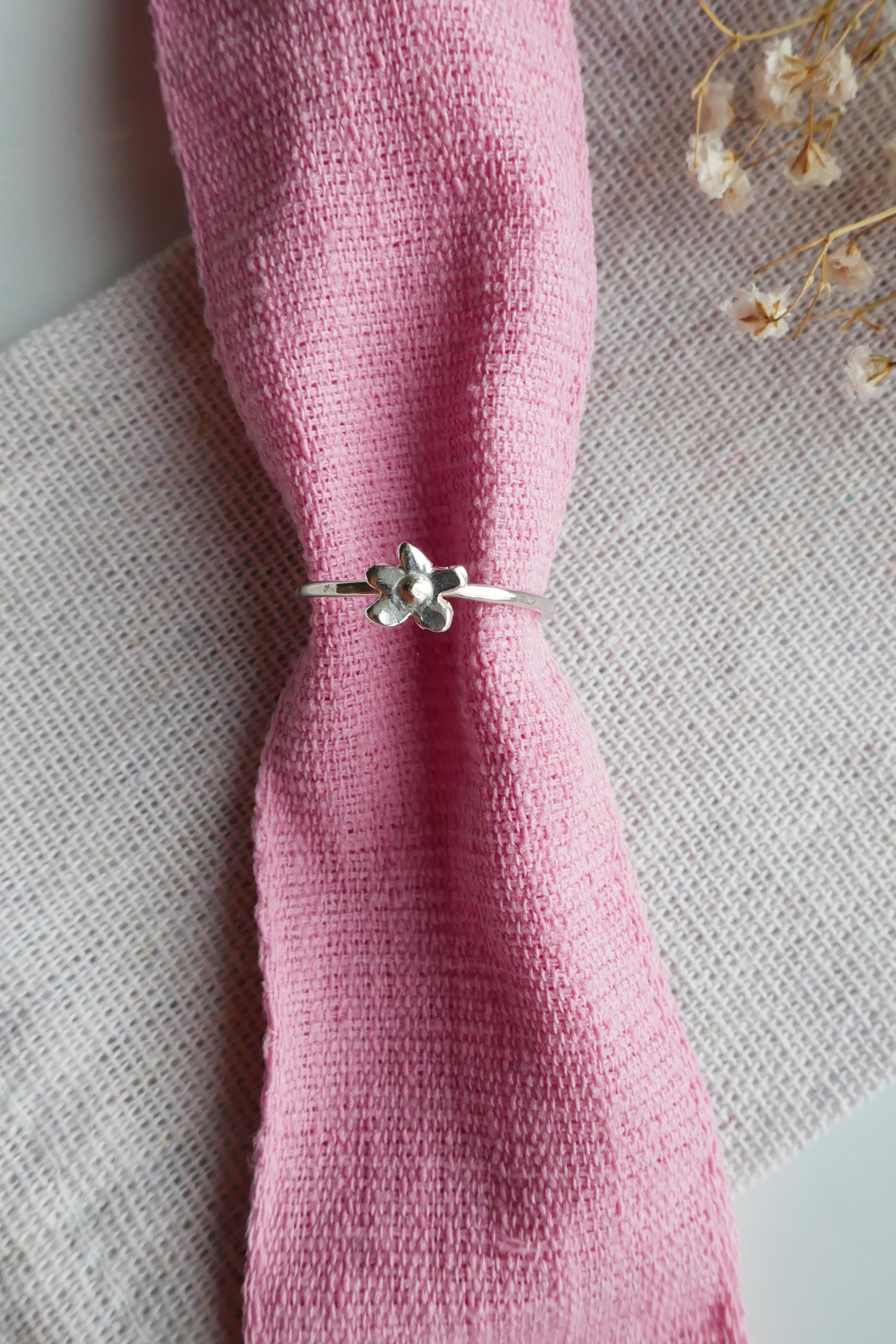 Silver ring with floral design on a pink napkin against a textured surface.