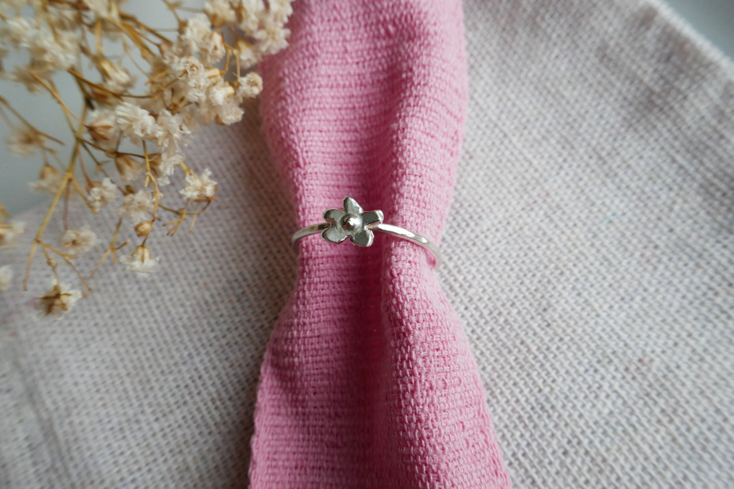 Silver ring with floral design on a pink fabric background