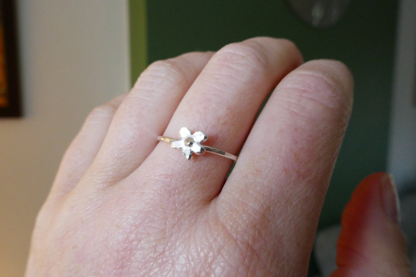 Hand wearing a delicate flower-shaped ring with a blurred background
