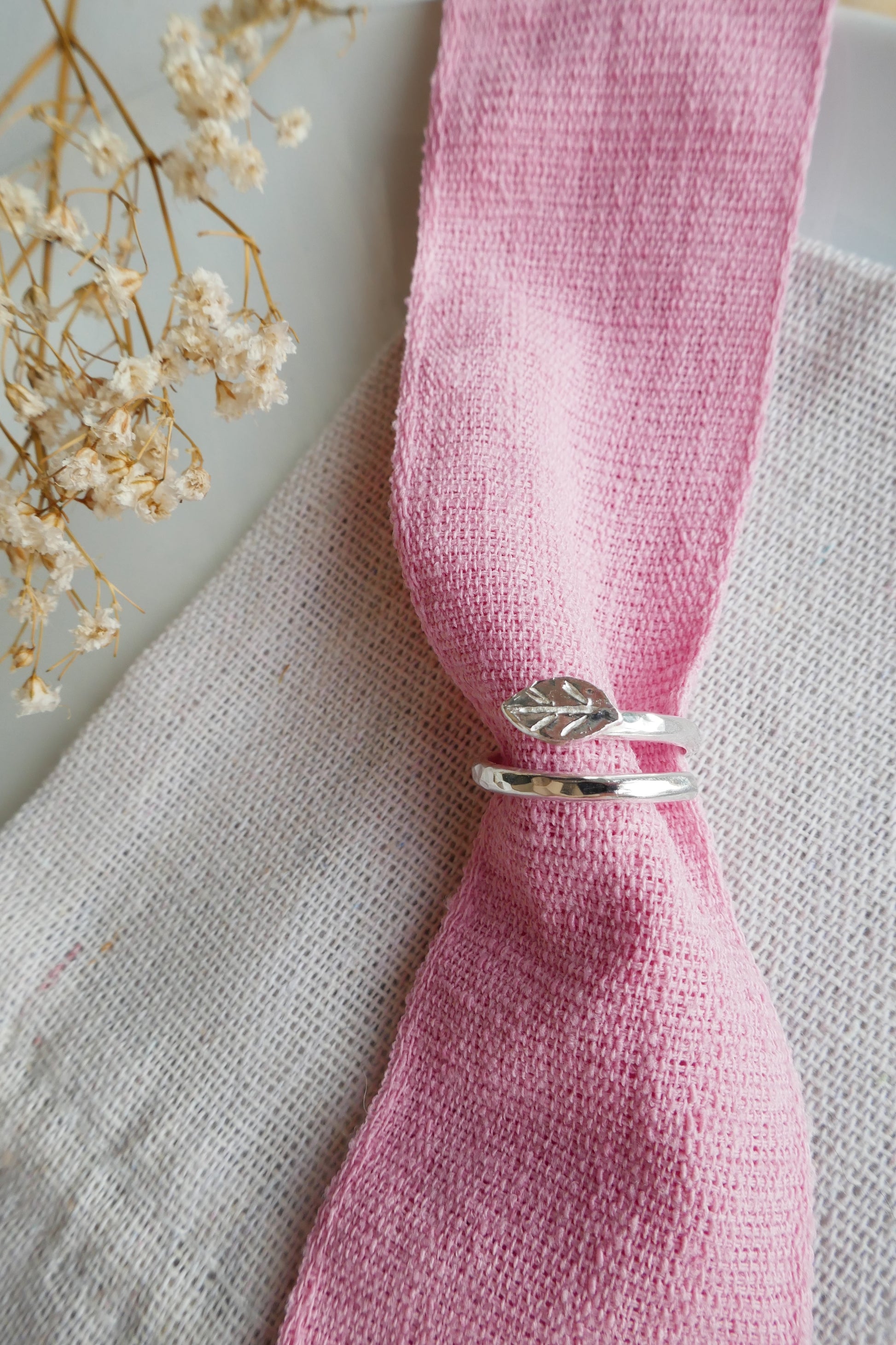 Silver ring with leaf design on a pink napkin with a light background