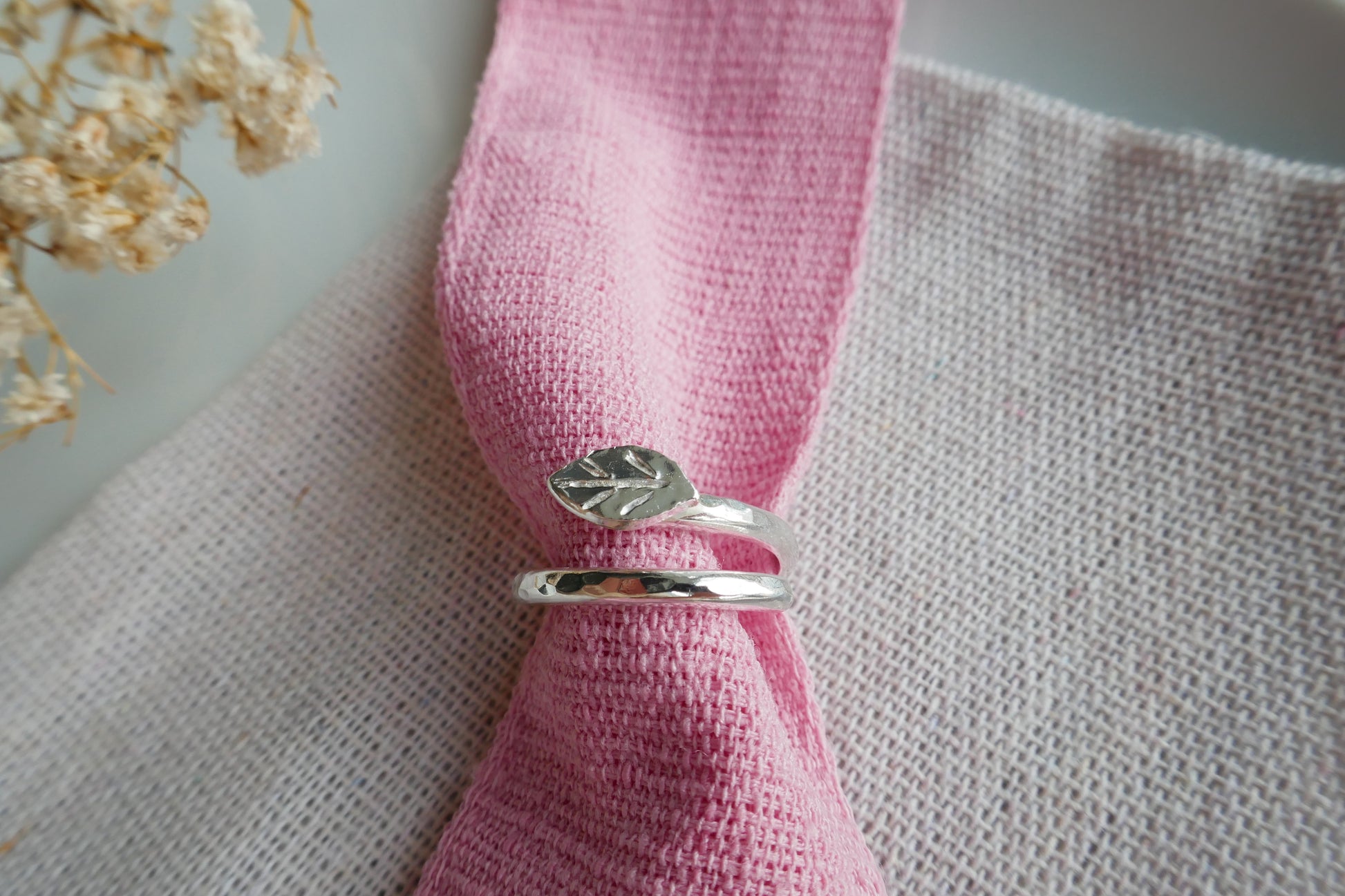 Silver ring with leaf design on a pink napkin with a blurred background