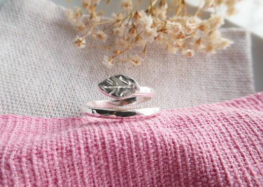 Silver leaf ring on a pink textured surface with dried flowers in the background