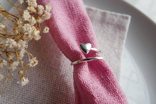 Silver heart-shaped napkin ring on a pink napkin with dried flowers.