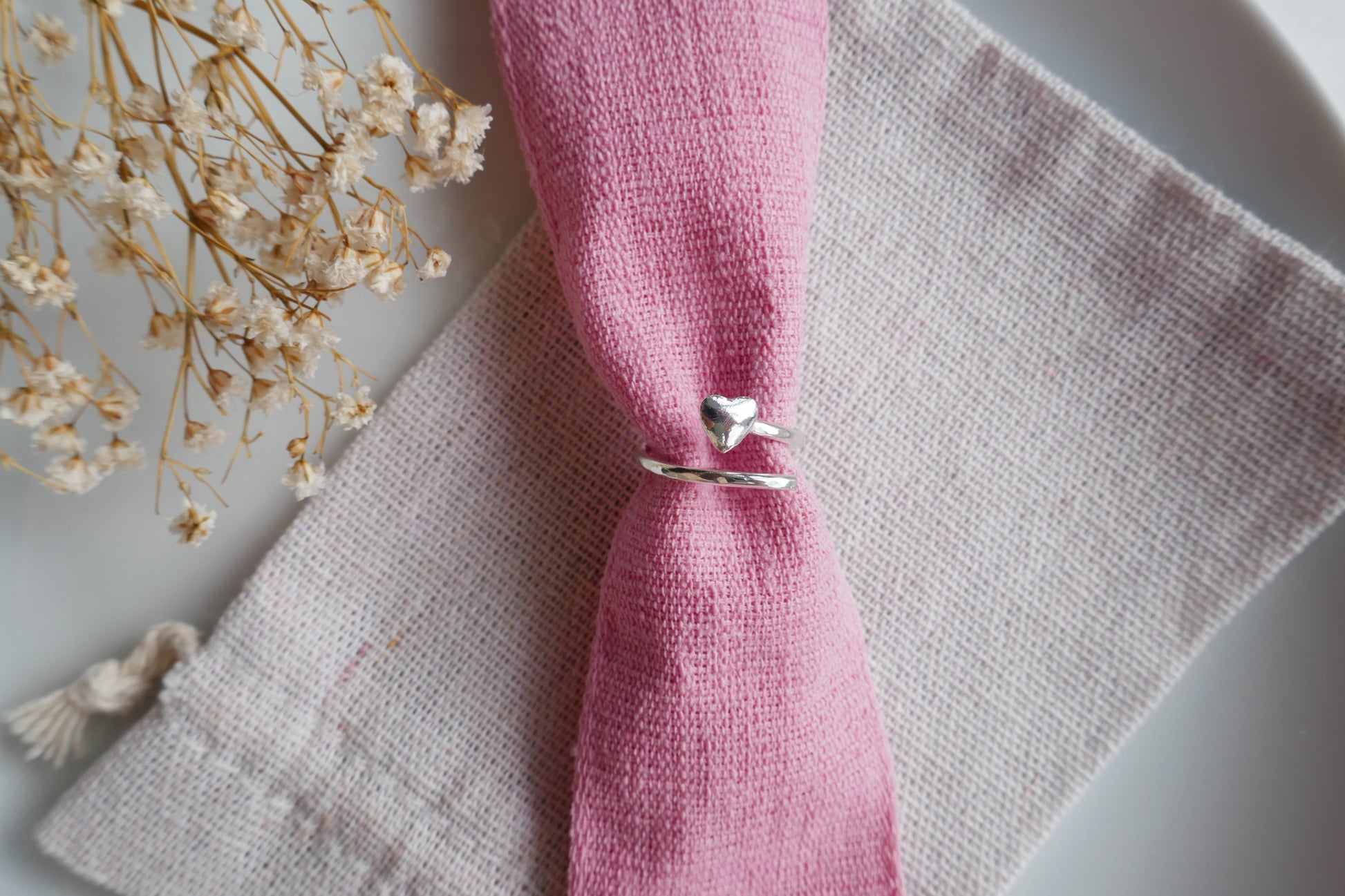 Silver ring on a pink fabric with dried flowers on a white background