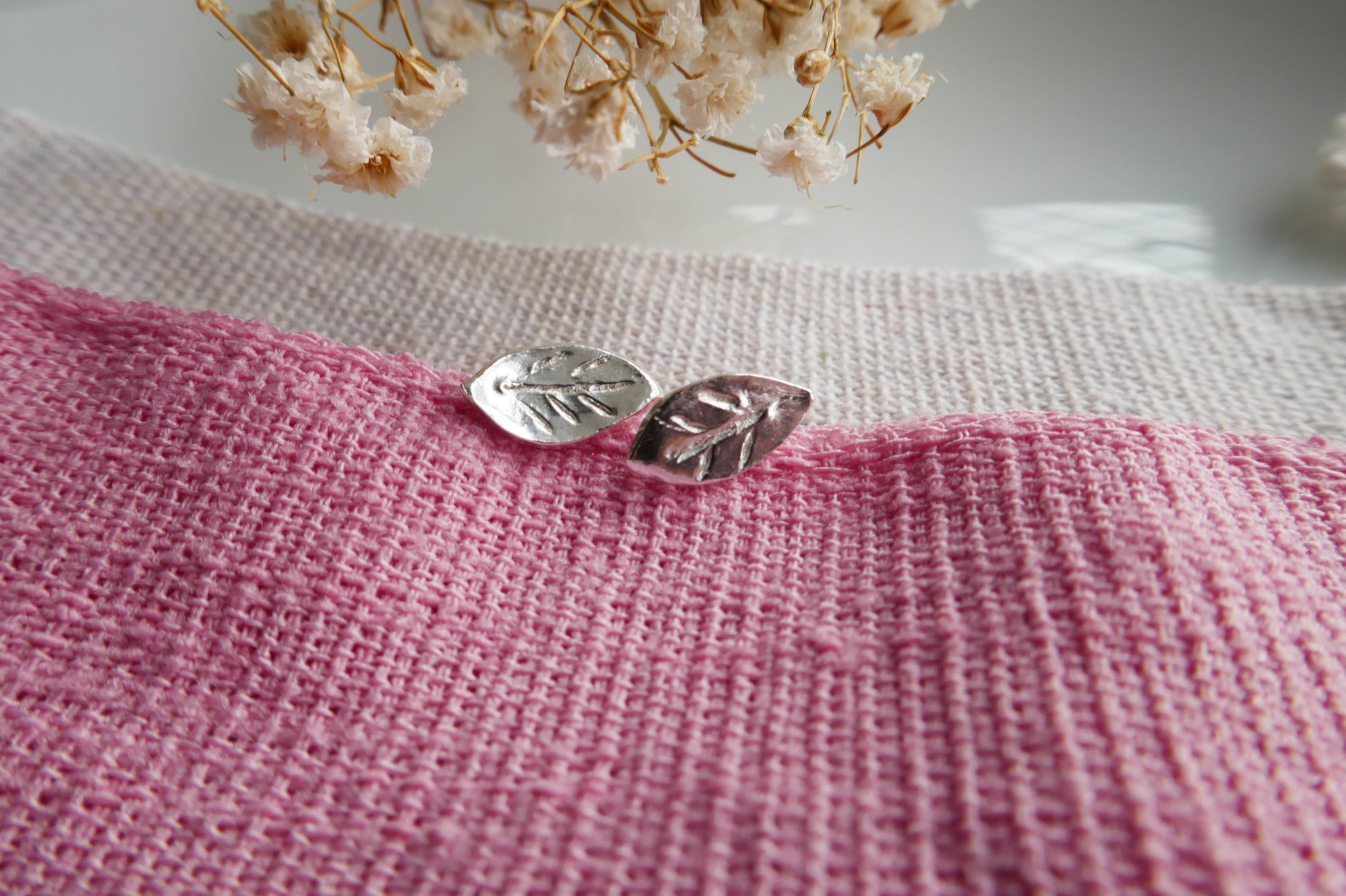 Silver leaf-shaped earrings on a pink and white textured fabric background