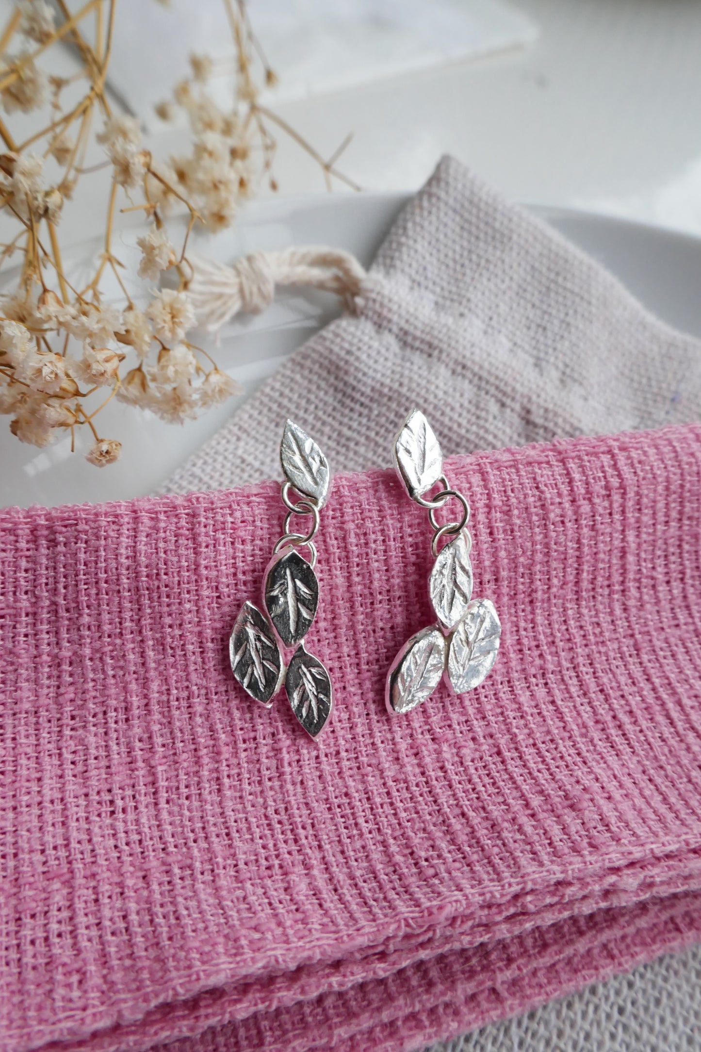Silver leaf earrings on a pink fabric background