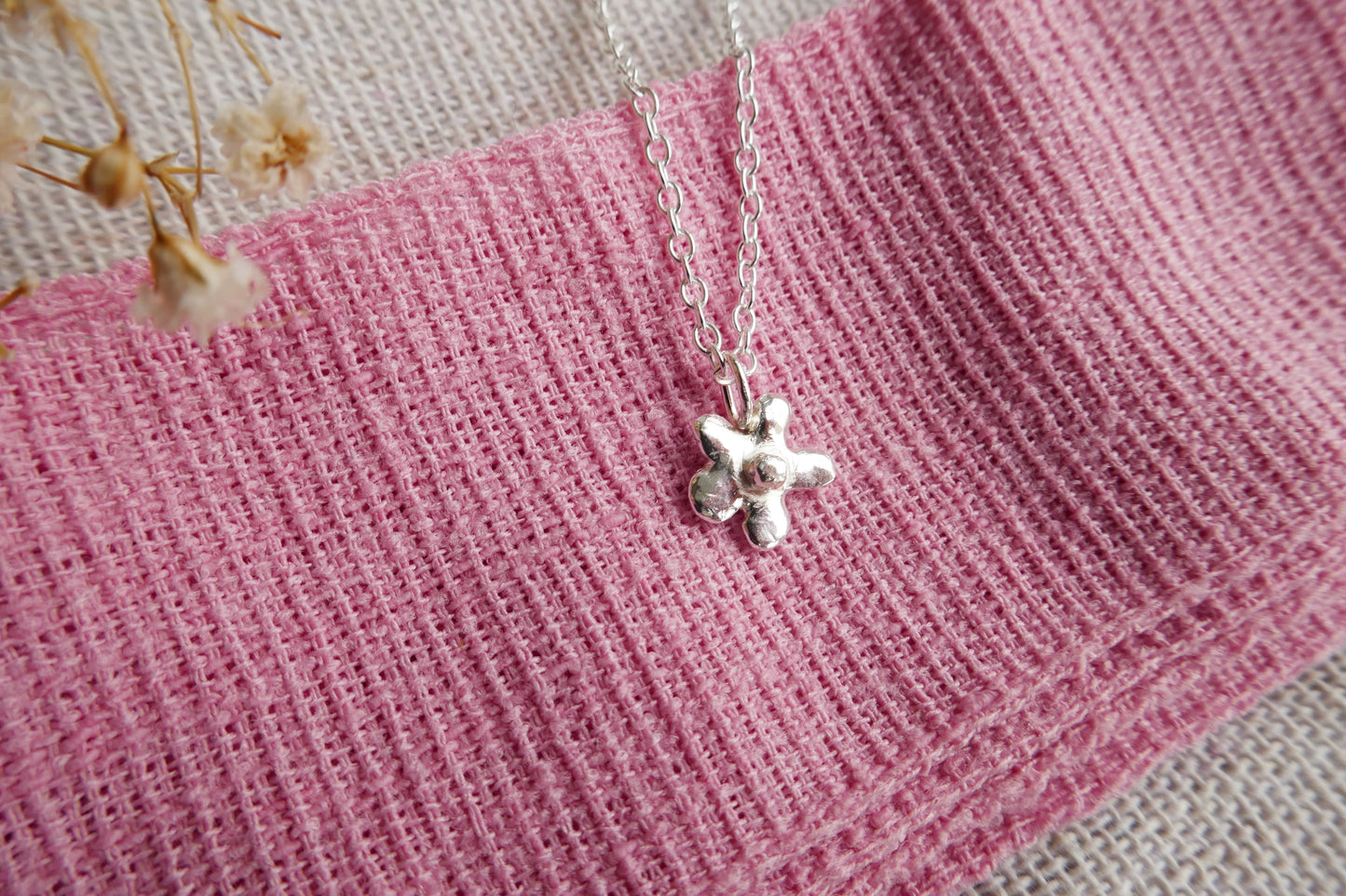 Silver necklace with a star pendant on a pink textured fabric background