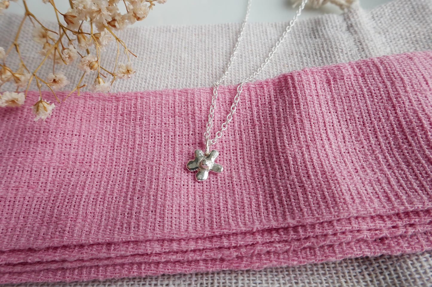 Silver necklace with a flower print pendant on a pink fabric background