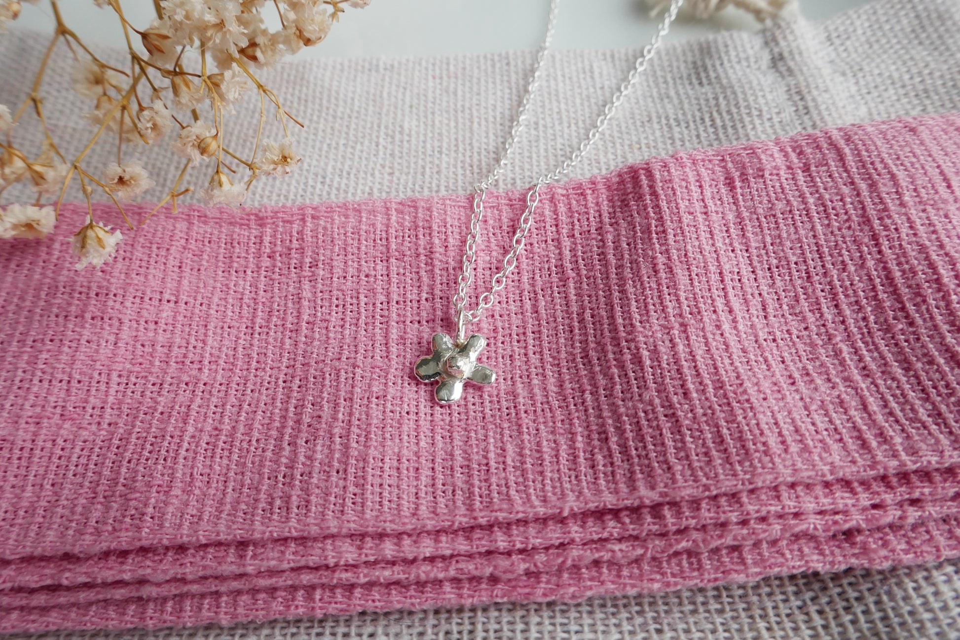 Silver necklace with a flower print pendant on a pink fabric background