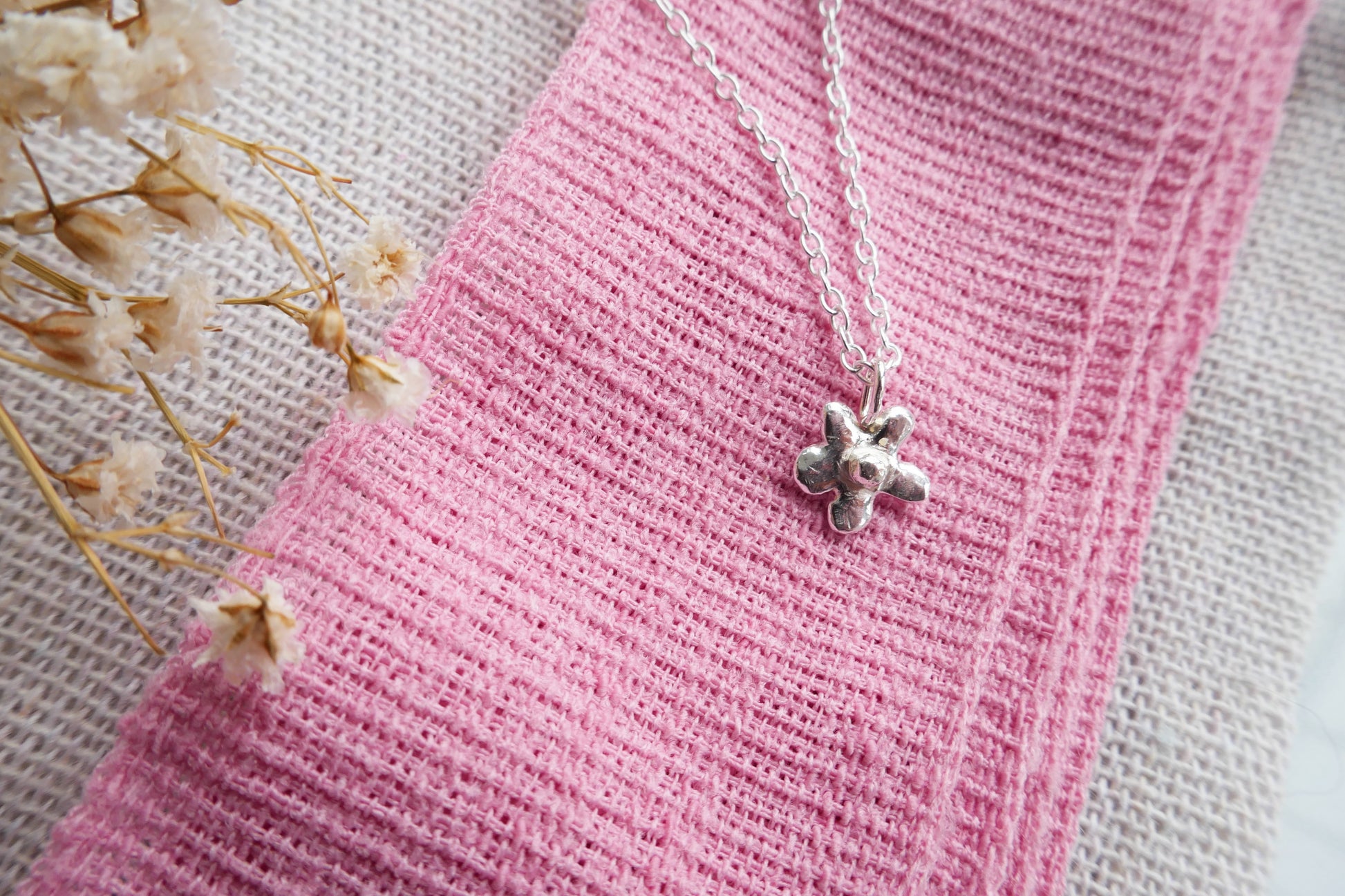 Silver necklace with a clover pendant on pink fabric with dried flowers.