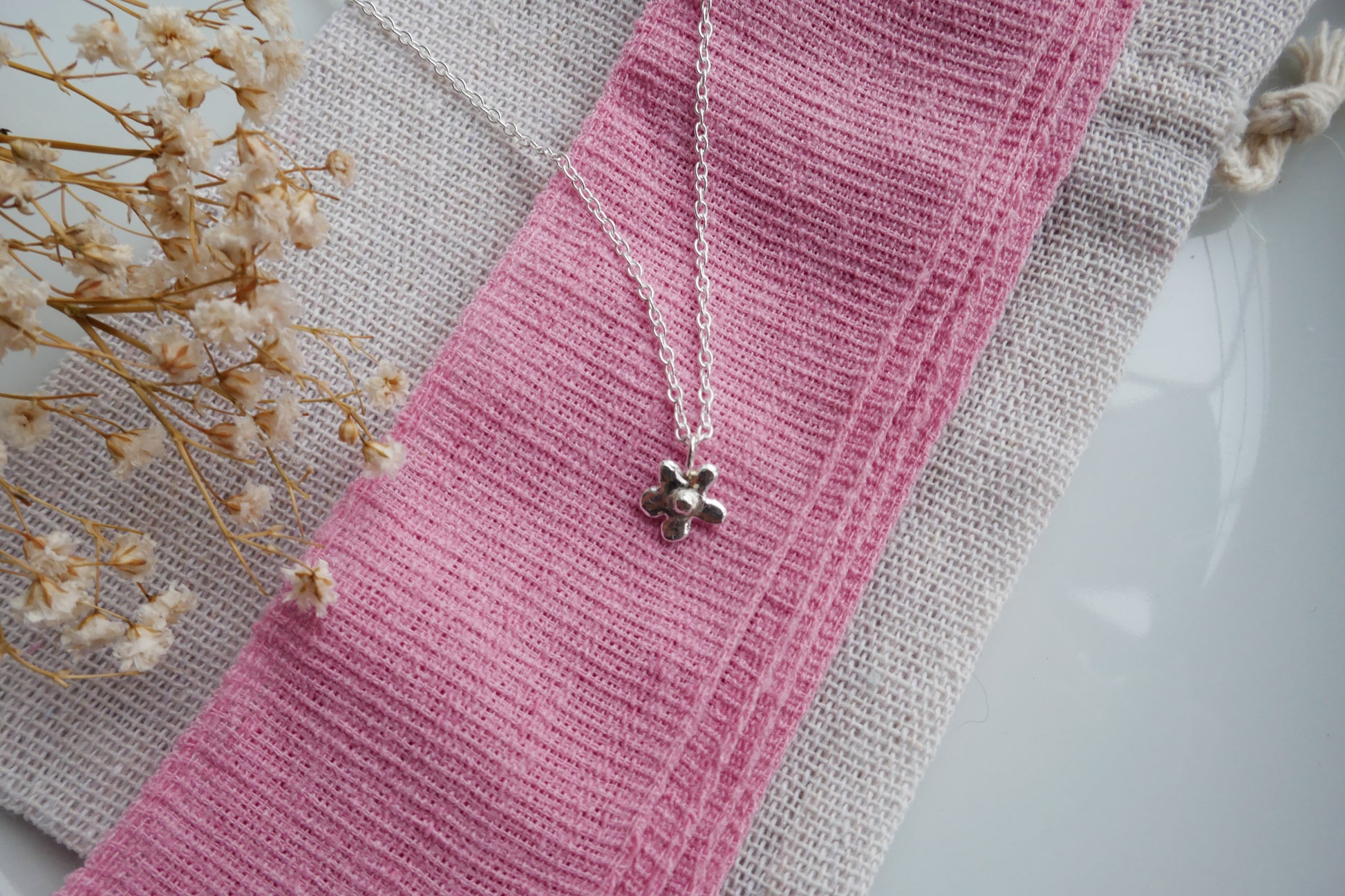 Silver necklace with a pendant on a pink fabric background with dried flowers.