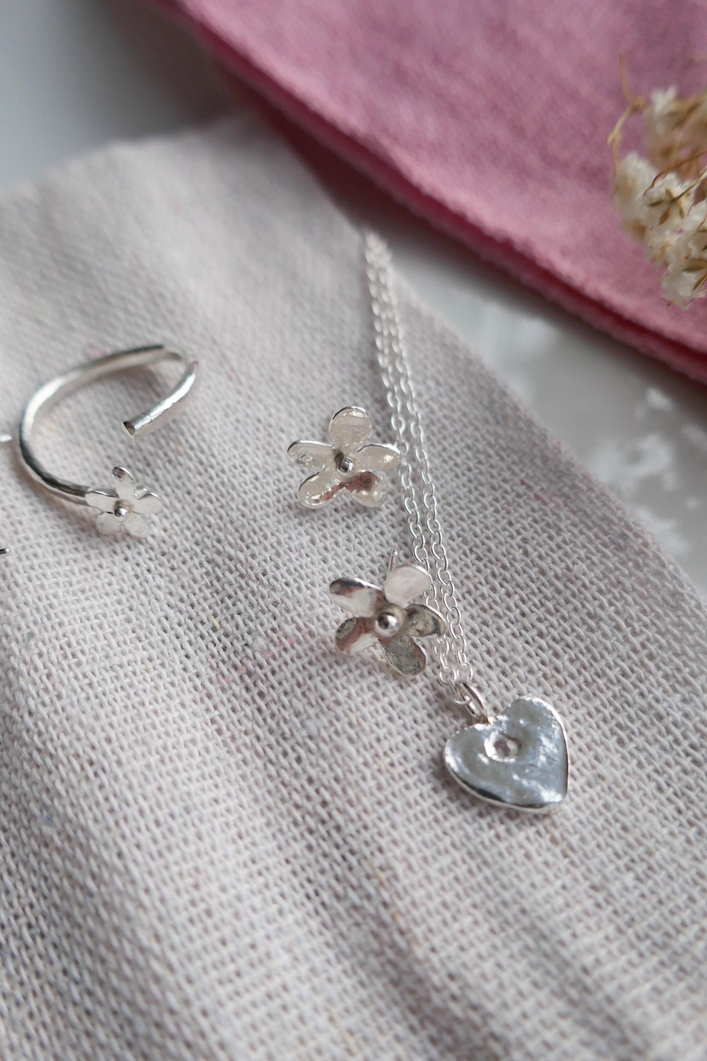 Silver jewelry set with floral pendant and heart charm on a textured fabric background