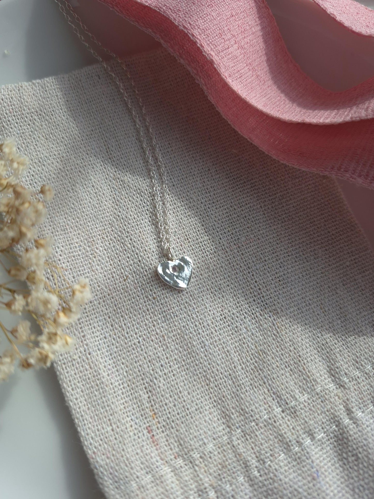 Silver heart-shaped pendant on a textured fabric background