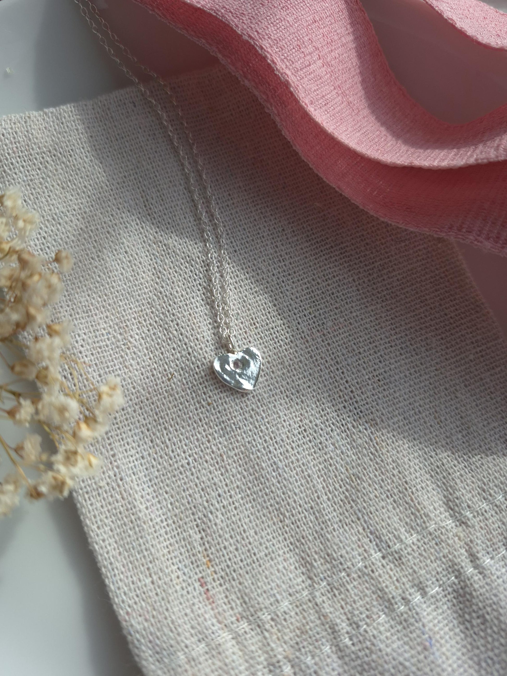 Silver heart-shaped pendant on a textured fabric background