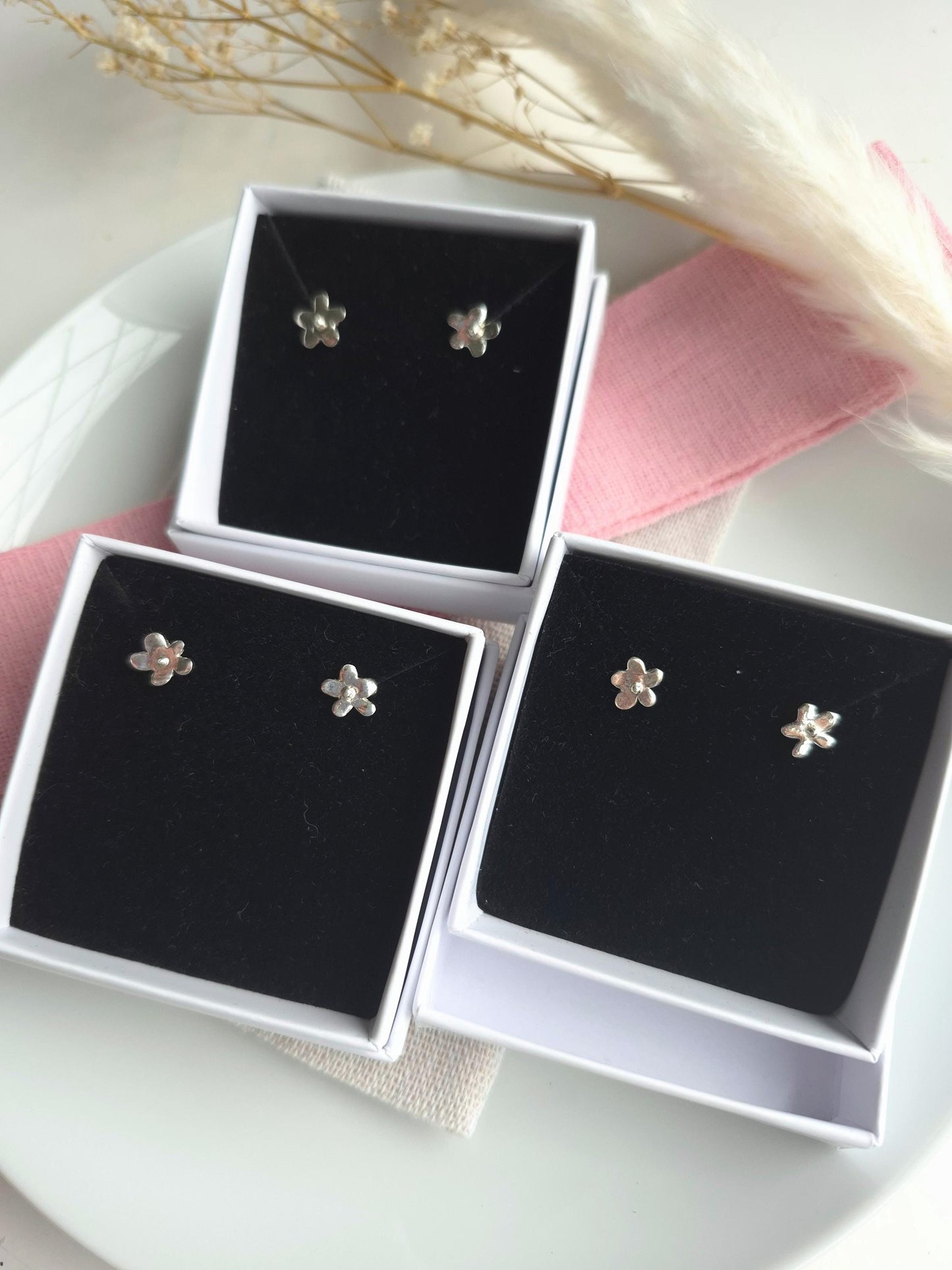 Flower-shaped earrings in a black display case on a white surface with pink fabric.