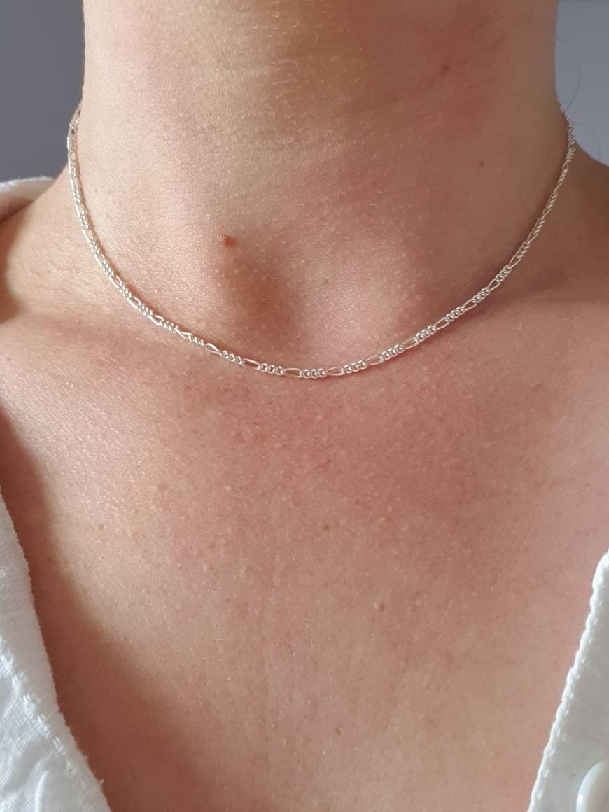 A neckline with a silver figaro chain. This chain has one larger link then three small links repeated. The chain is quite fine.