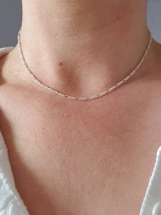 A neckline with a silver figaro chain. This chain has one larger link then three small links repeated. The chain is quite fine.